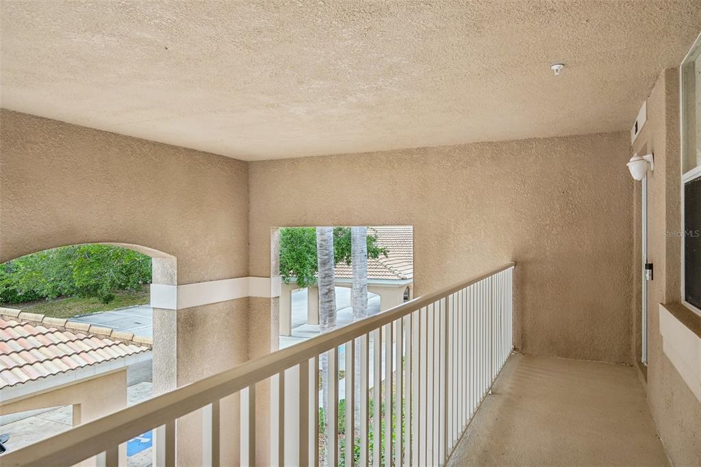 A covered balcony features beige stucco walls, a white metal railing, and views of rooftops — 1003 FAIRWAYCOVE LANE UNIT 201, BRADENTON, FL