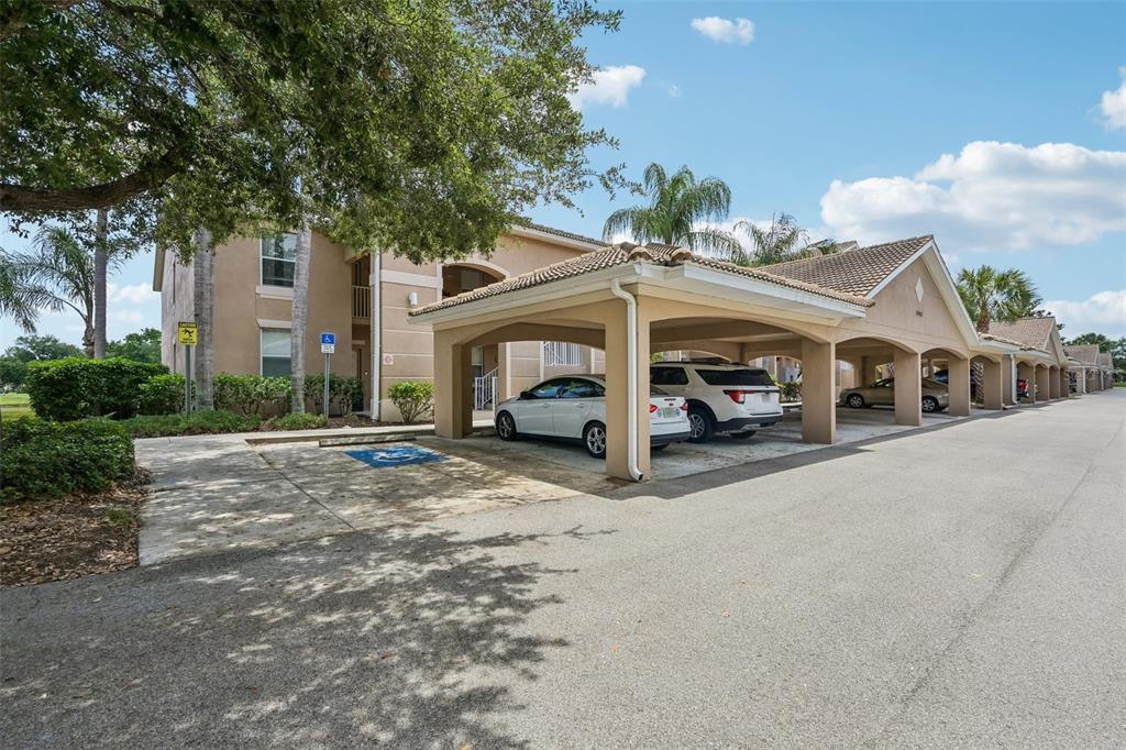 A multi-story apartment building features a covered parking area with several parked vehicles — 1003 FAIRWAYCOVE LANE UNIT 201, BRADENTON, FL