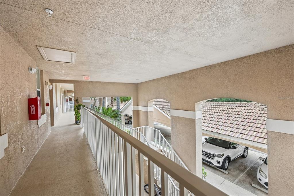 An outdoor apartment walkway features a white railing, stucco walls, and a view of parking — 1003 FAIRWAYCOVE LANE UNIT 201, BRADENTON, FL