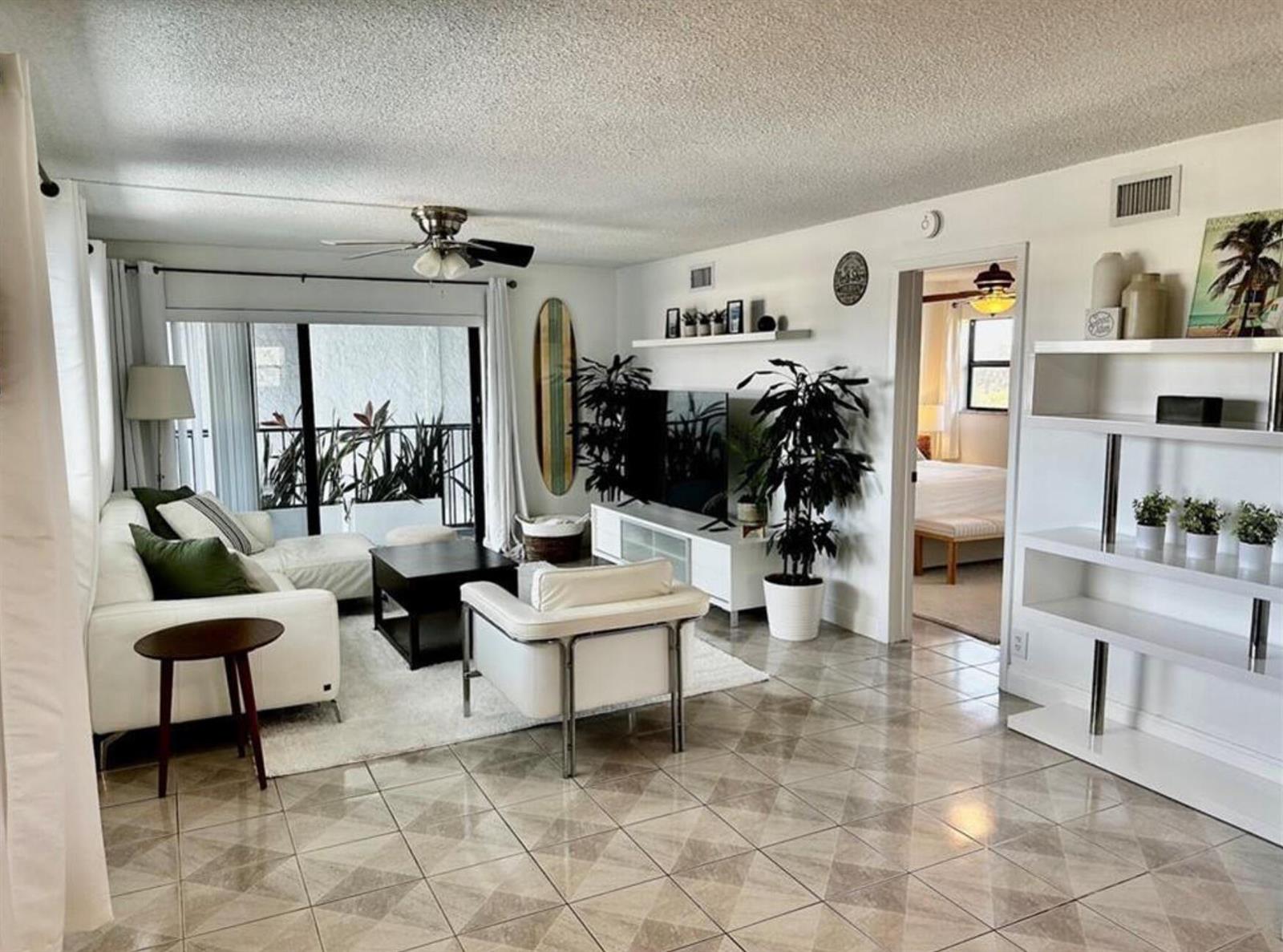 A living room with tile floors, a white sofa, a television, and a balcony view — 1975 SE 3rd Street # 403, Deerfield Beach FL 33441, DEERFIELD BEACH, FL