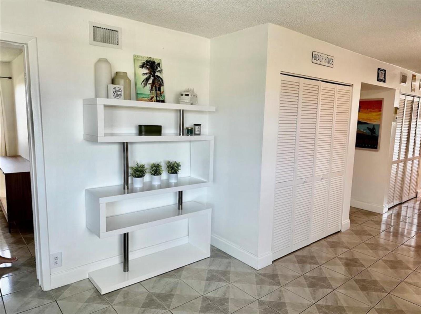 A white modern bookshelf stands against a wall next to white louvered closet doors — 1975 SE 3rd Street # 403, Deerfield Beach FL 33441, DEERFIELD BEACH, FL