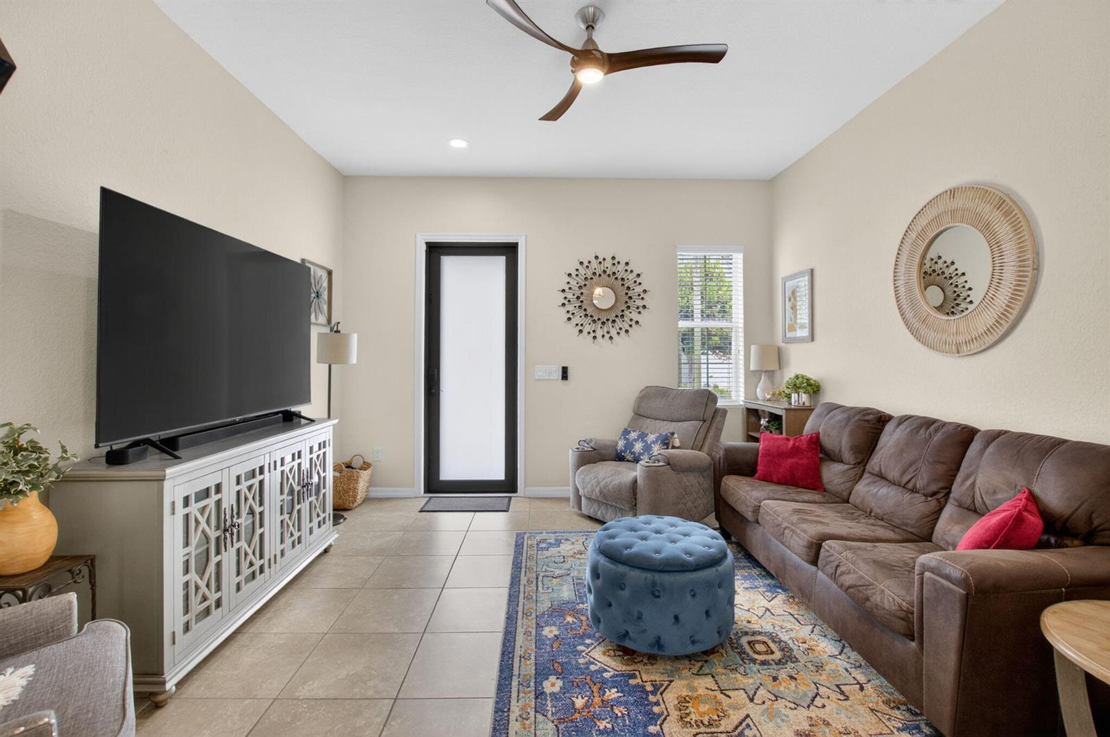 A living room features a large television, brown sofa, blue ottoman, and tiled flooring — 485 Graham Place, Boynton Beach FL 33435, BOYNTON BEACH, FL