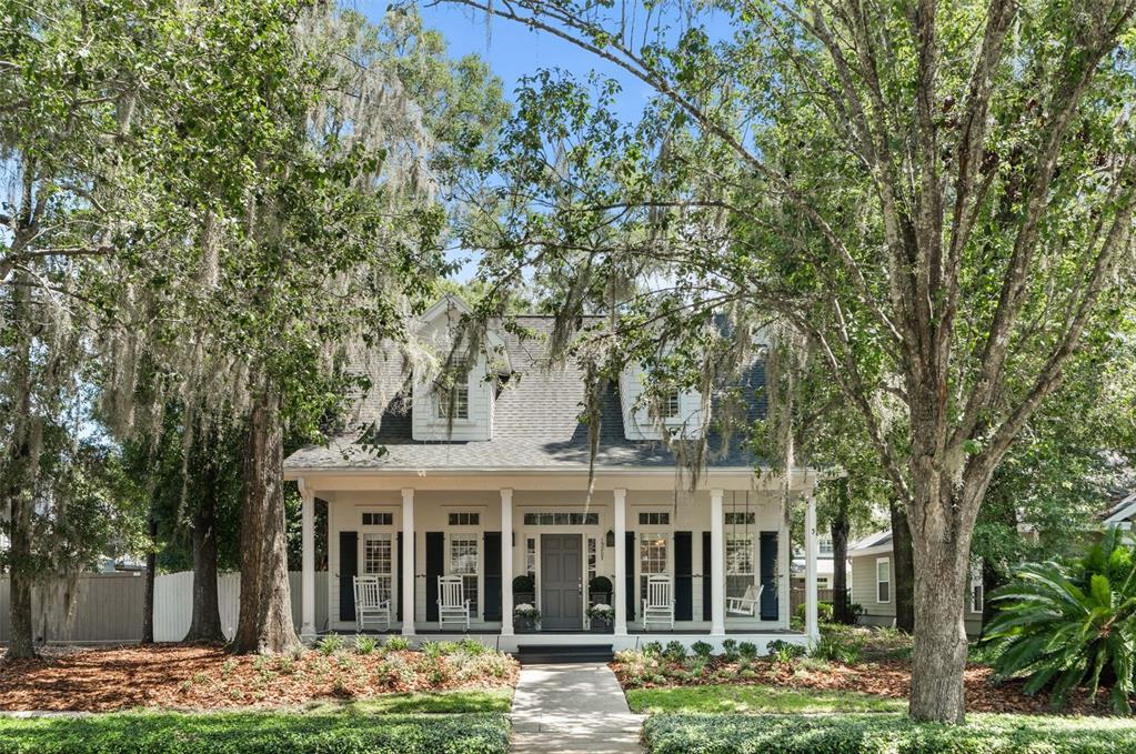 A two-story house with a front porch, dormer windows, and dark shutters sits among trees — 13207 SW 2ND AVENUE, NEWBERRY, FL