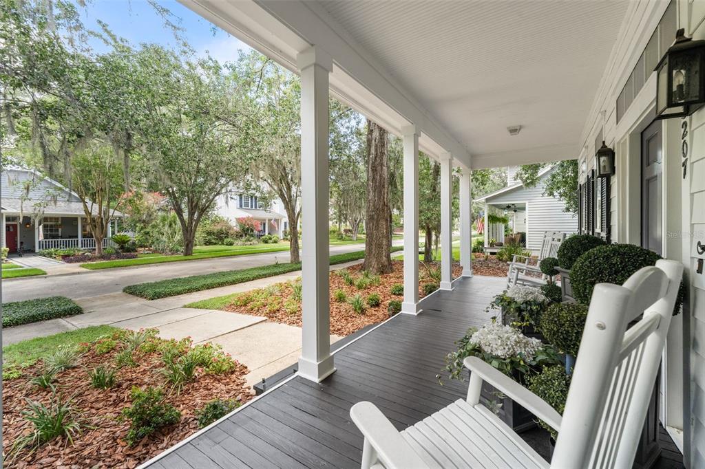 A covered front porch with white rocking chairs overlooks a tree-lined residential street — 13207 SW 2ND AVENUE, NEWBERRY, FL