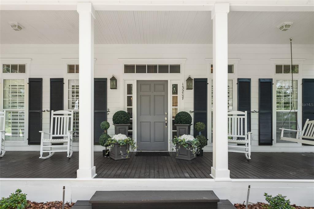 A front porch features a gray door, white rocking chairs, a porch swing, and dark wood flooring — 13207 SW 2ND AVENUE, NEWBERRY, FL