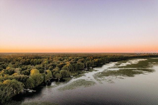 An aerial view shows a lake bordered by a dense forest under a sunset sky — 13821 SE 202ND TERRACE, HAWTHORNE, FL