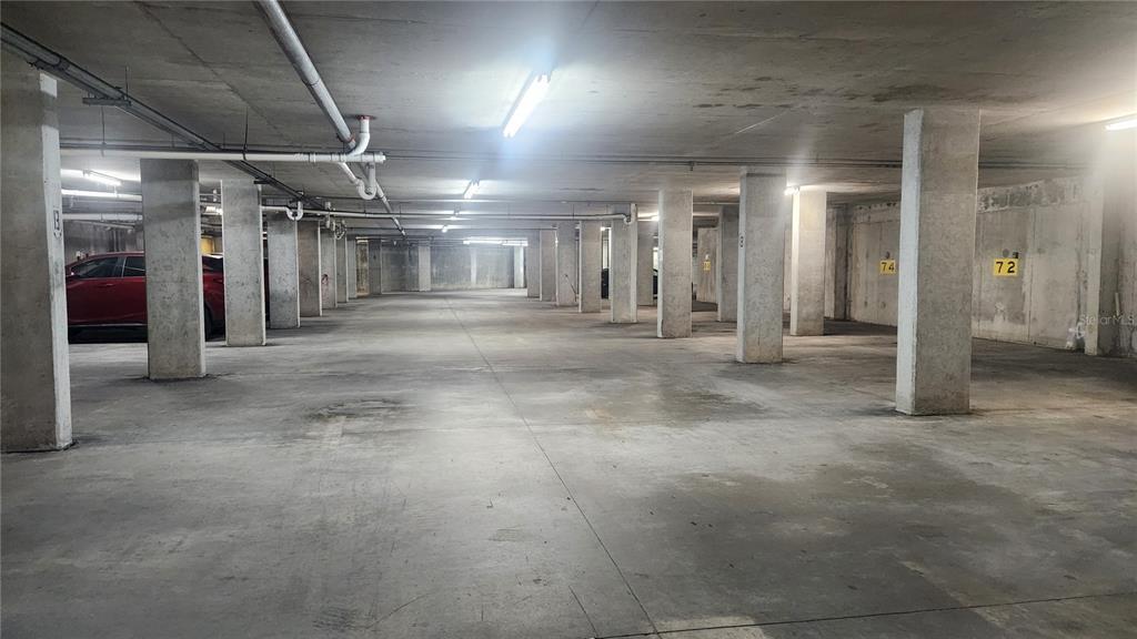 An indoor parking garage features concrete columns, overhead pipes, and numbered parking spaces — 101 PALM HARBOR PARKWAY UNIT P066, PALM COAST, FL