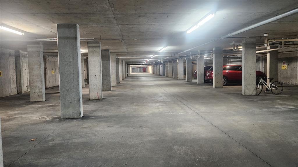 A concrete parking garage features support pillars, overhead lighting, and a parked red car — 101 PALM HARBOR PARKWAY UNIT P066, PALM COAST, FL