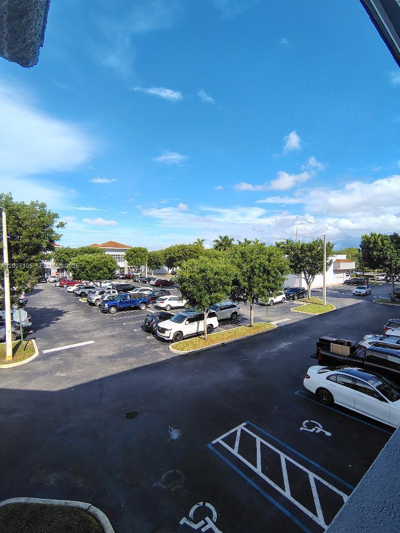 An elevated view of a parking lot with numerous cars and trees under a blue sky — 14285 SW 42nd St # 211, Miami FL 33175, MIAMI, FL