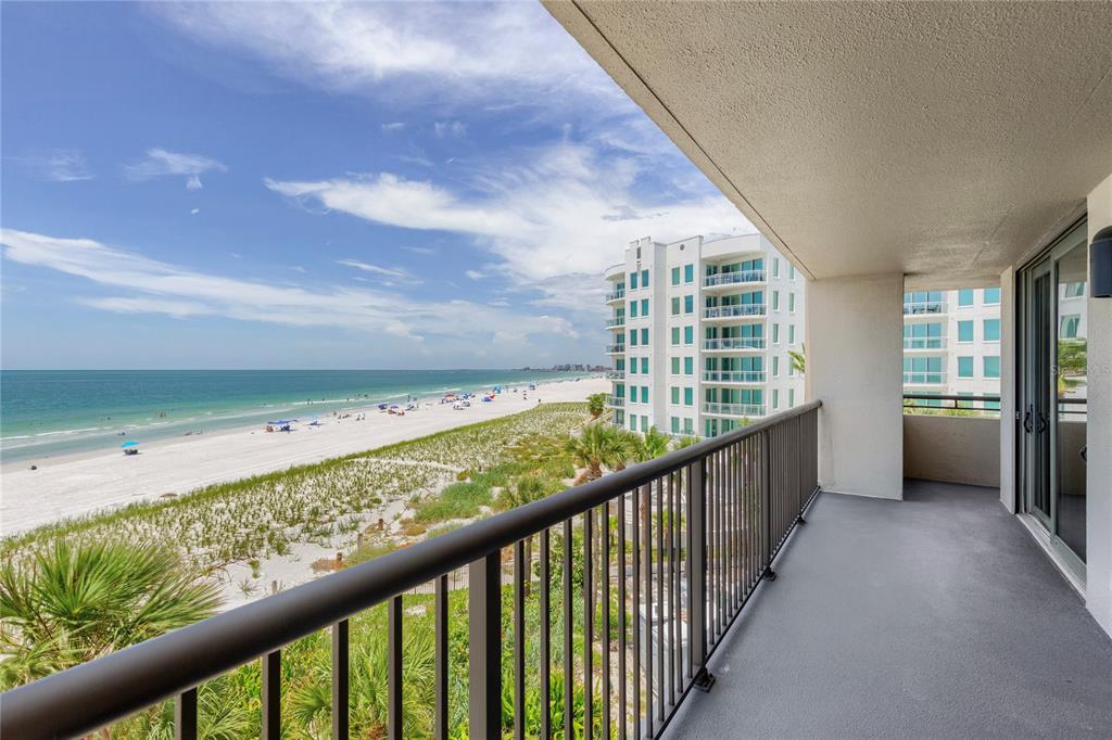 A balcony with a metal railing overlooks a sandy beach, ocean, and a neighboring building — 1600 GULF BOULEVARD UNIT 414, CLEARWATER, FL