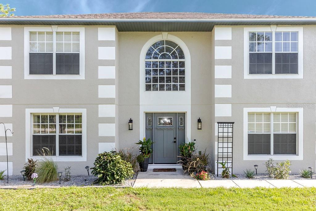 A two-story house exterior features a gray front door, arched window, and white trim accents — 11083 MAYBIRD AVENUE, WEEKI WACHEE, FL