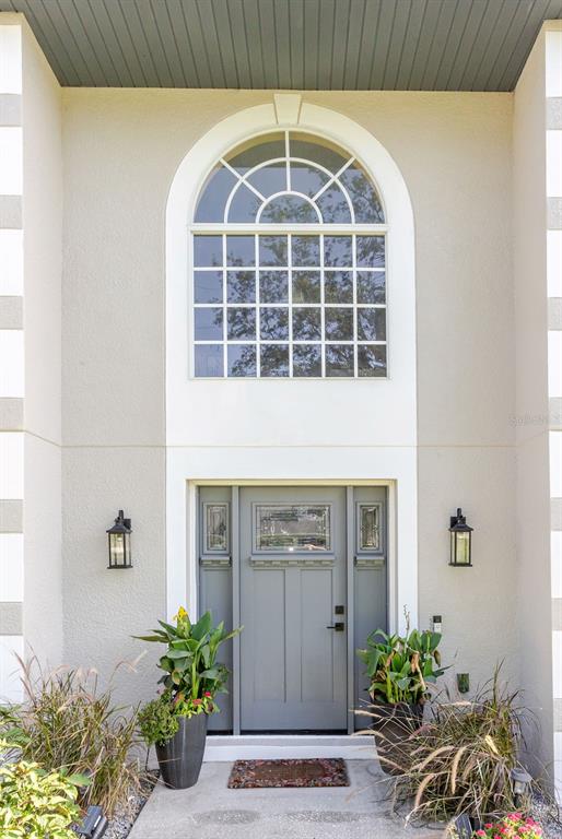 A gray front door with sidelights sits beneath an arched window on a stucco exterior — 11083 MAYBIRD AVENUE, WEEKI WACHEE, FL