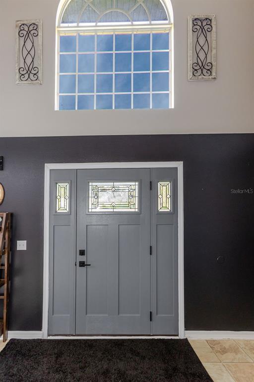 A gray front door with sidelights sits below a large arched window in an entryway — 11083 MAYBIRD AVENUE, WEEKI WACHEE, FL