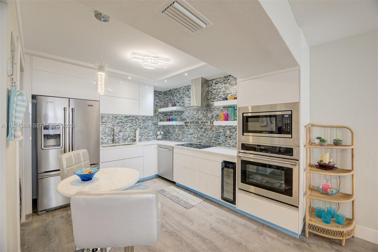 A modern kitchen features white cabinetry, stainless steel appliances, and a blue mosaic tile backsplash — 3725 S Ocean Dr # 601, Hollywood FL 33019, HOLLYWOOD, FL