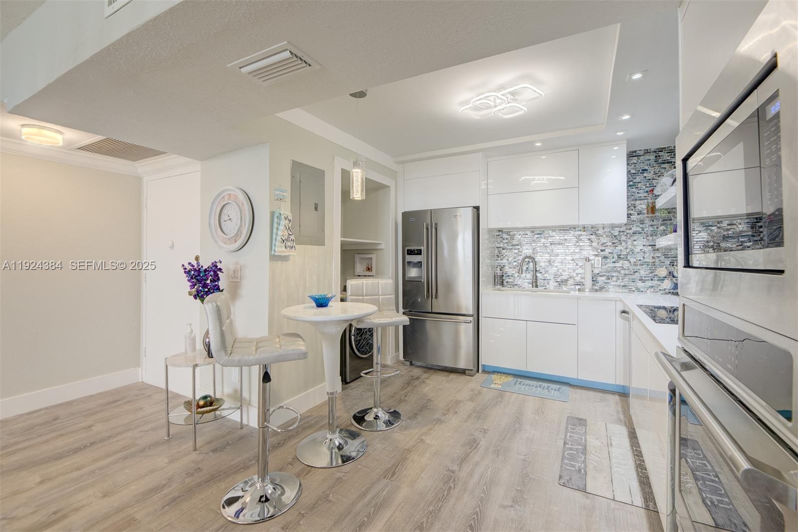 A modern kitchen features white cabinetry, stainless steel appliances, and a small bistro dining set — 3725 S Ocean Dr # 601, Hollywood FL 33019, HOLLYWOOD, FL