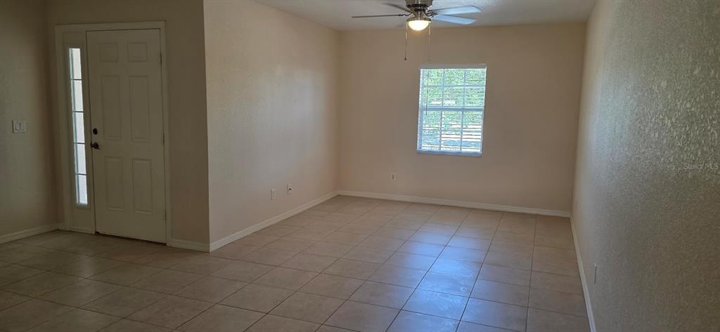 An empty room with beige tile flooring, a ceiling fan, and a front entry door — 26201 EXPLORER ROAD UNIT 5, PUNTA GORDA, FL