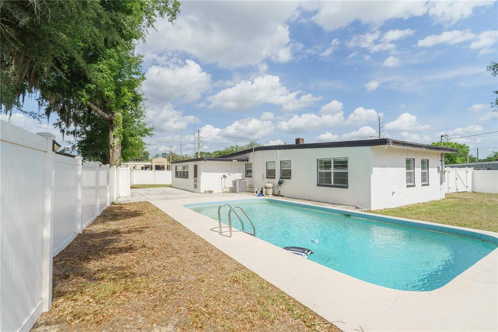 A backyard features a rectangular swimming pool, a white vinyl fence, and a white house — 3523 SE 6TH STREET, OCALA, FL