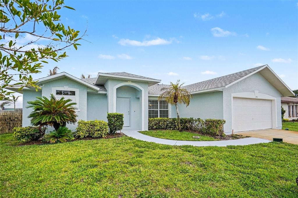 A light blue single-story house features a front-facing garage, arched entryway, and landscaped front yard — 380 SHERIDAN AVENUE, SATELLITE BEACH, FL