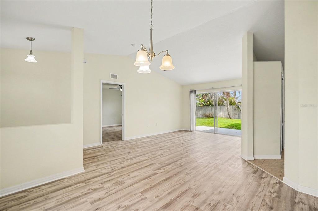 A bright, empty living room features light wood-look flooring, a vaulted ceiling, and sliding doors — 380 SHERIDAN AVENUE, SATELLITE BEACH, FL