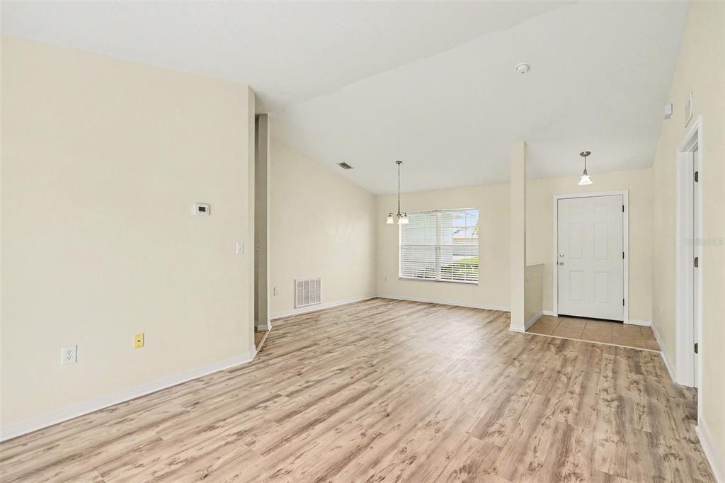 An empty living and dining area with light wood-look flooring and a white front door — 380 SHERIDAN AVENUE, SATELLITE BEACH, FL