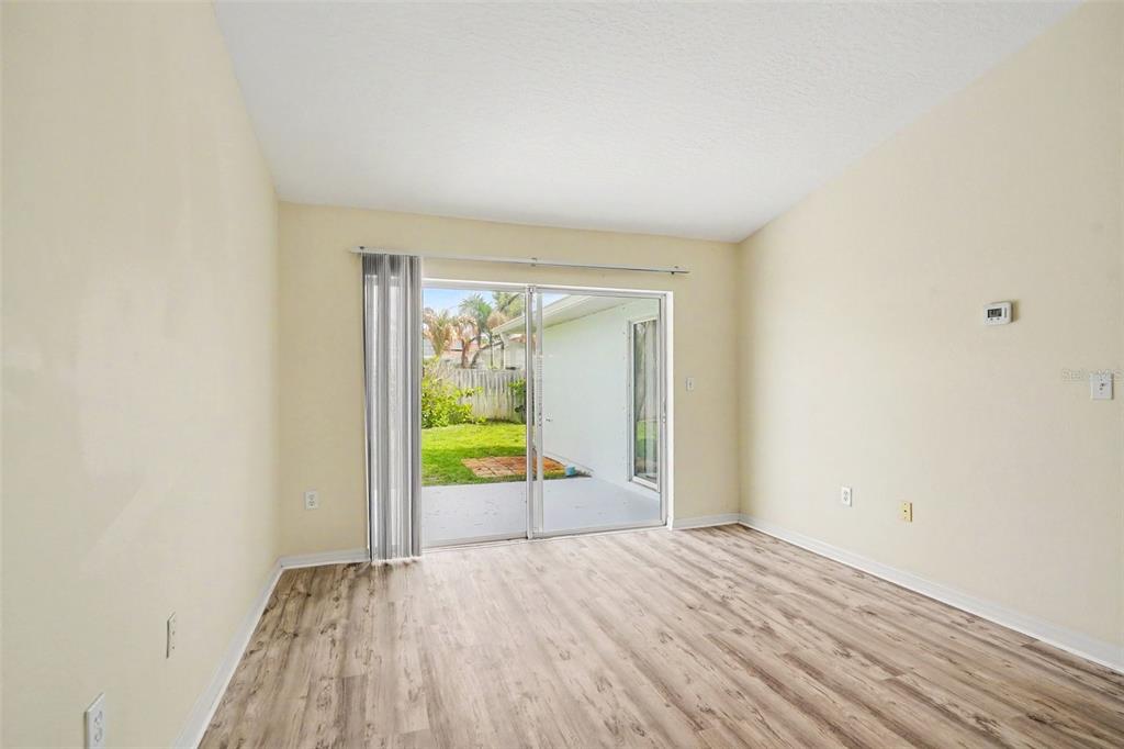 An empty room with light wood-look flooring and sliding glass doors leading to a patio — 380 SHERIDAN AVENUE, SATELLITE BEACH, FL