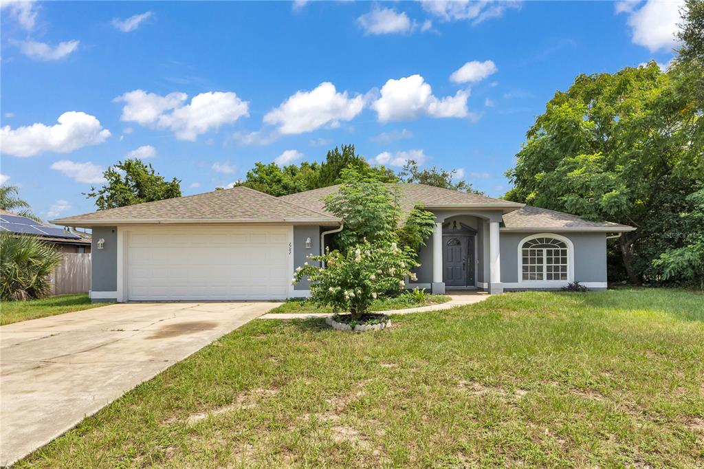 A single-story gray house with a two-car garage and a front yard under a blue sky — 2752 N JULIET DRIVE, DELTONA, FL