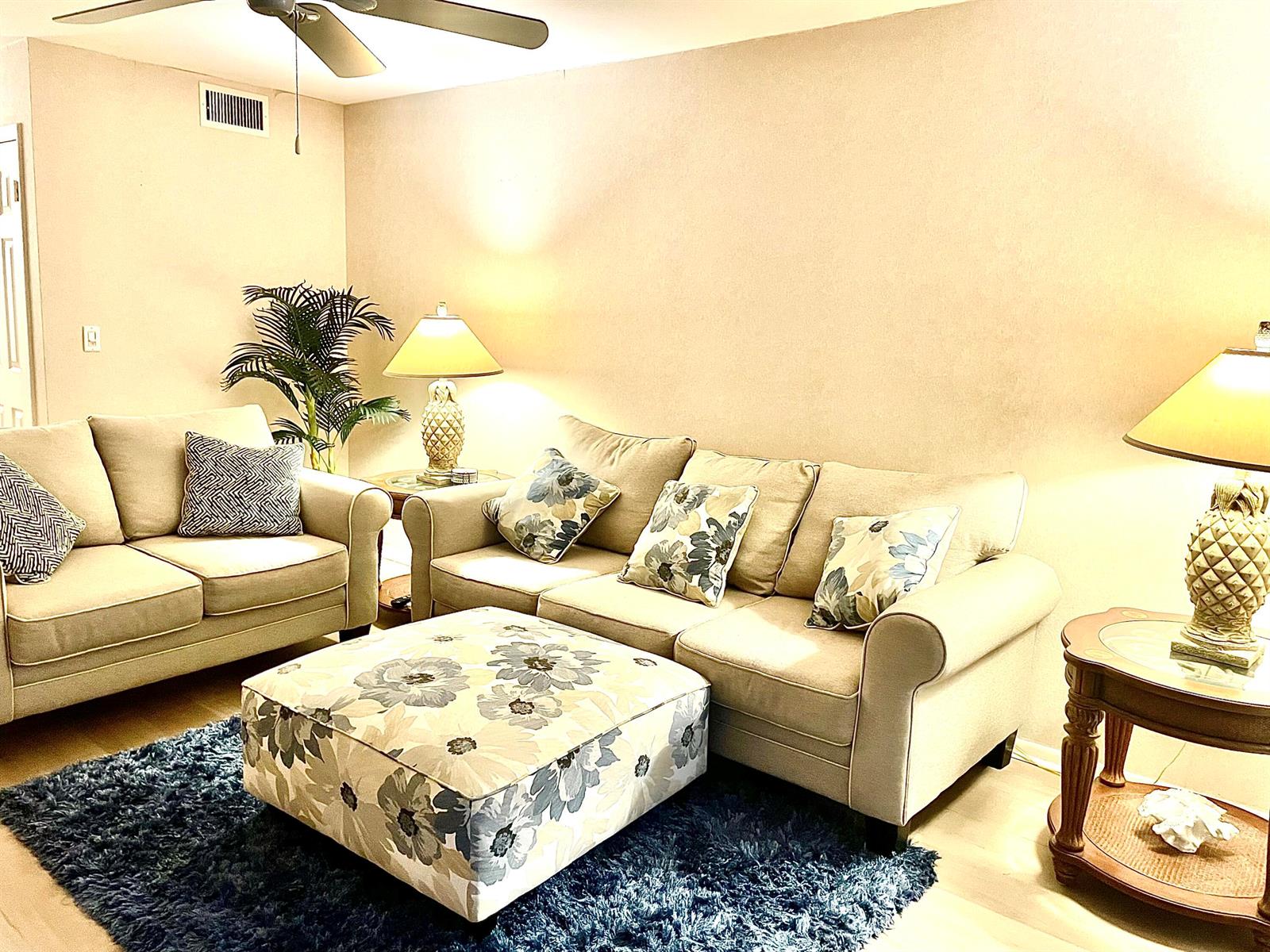 A living room features beige sofas, a floral ottoman, a blue rug, and pineapple lamps — 2929 SE Ocean Boulevard # 117, Stuart FL 34996, STUART, FL