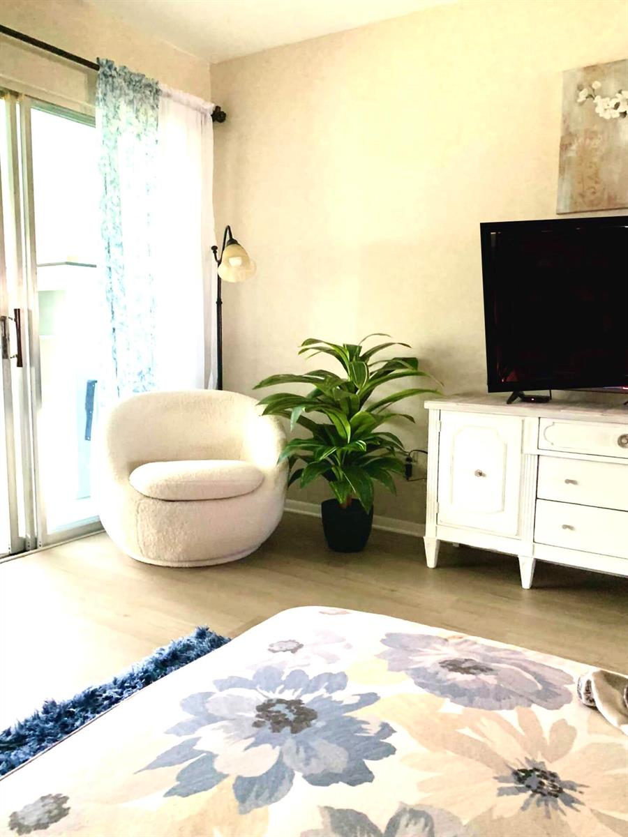 A living room features a white armchair, a potted plant, and a television on a cabinet — 2929 SE Ocean Boulevard # 117, Stuart FL 34996, STUART, FL