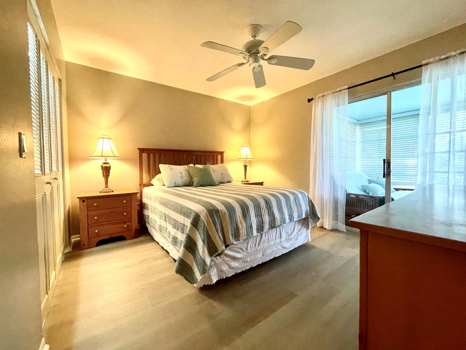 A bedroom features a wooden bed, two nightstands with lamps, and a sliding glass door — 2929 SE Ocean Boulevard # 117, Stuart FL 34996, STUART, FL