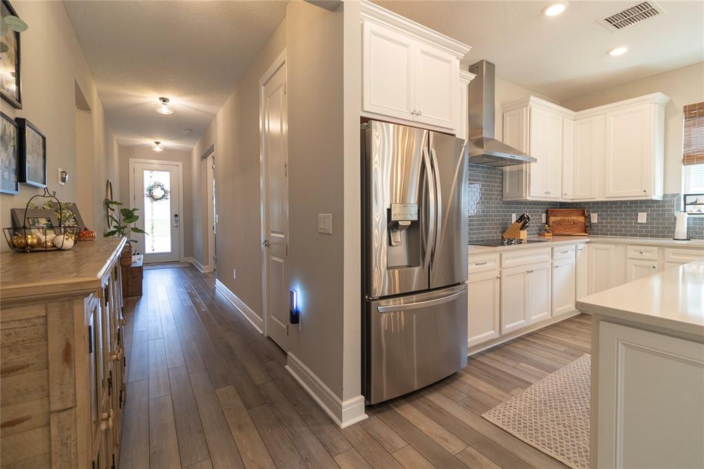 A kitchen with white cabinets and stainless steel appliances opens into a hallway with wood flooring — 12951 BROOKSIDE MOSS DRIVE, RIVERVIEW, FL