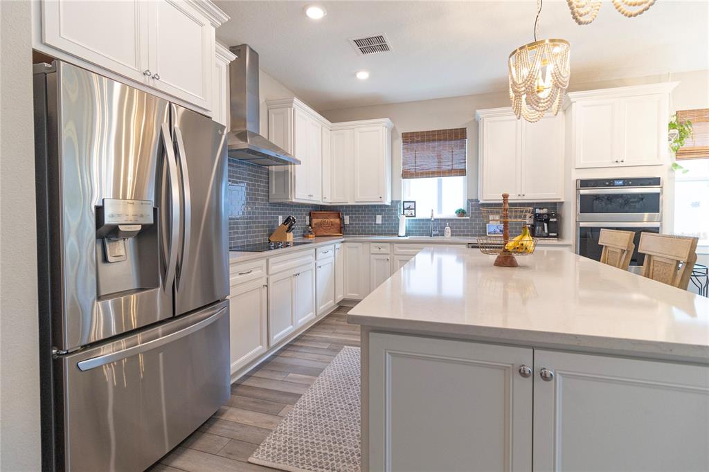 A modern kitchen features white cabinets, stainless steel appliances, a large island, and gray backsplash — 12951 BROOKSIDE MOSS DRIVE, RIVERVIEW, FL