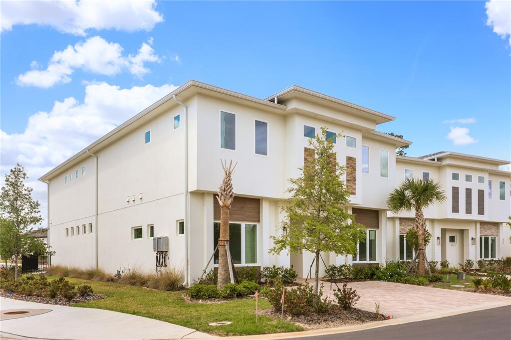 A modern two-story white stucco townhouse with a paver driveway and small palm trees — 7638 WHITEMARSH WAY, KISSIMMEE, FL