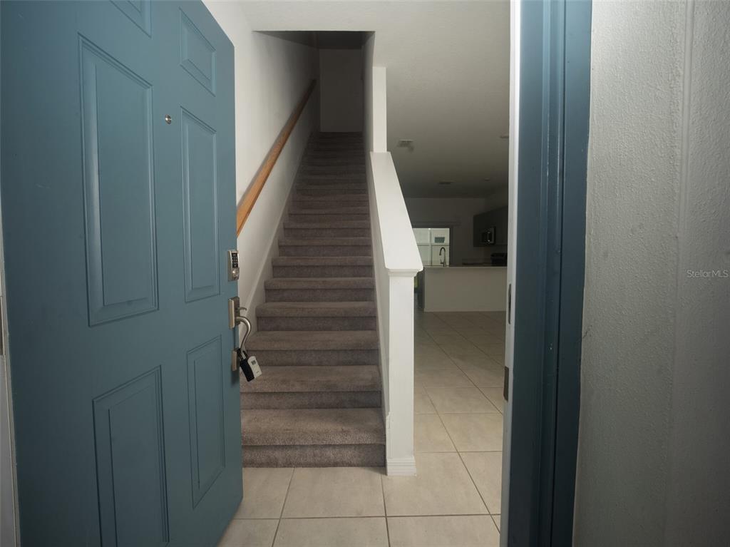 An open blue door reveals a carpeted staircase leading upward next to a tiled entryway — 3208 SKYLINE LOOP, POINCIANA, FL