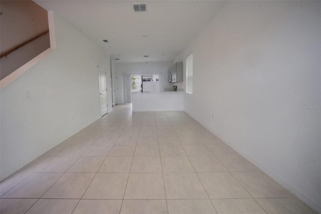 An empty room with white walls, tile flooring, and a kitchen area in the back — 3208 SKYLINE LOOP, POINCIANA, FL