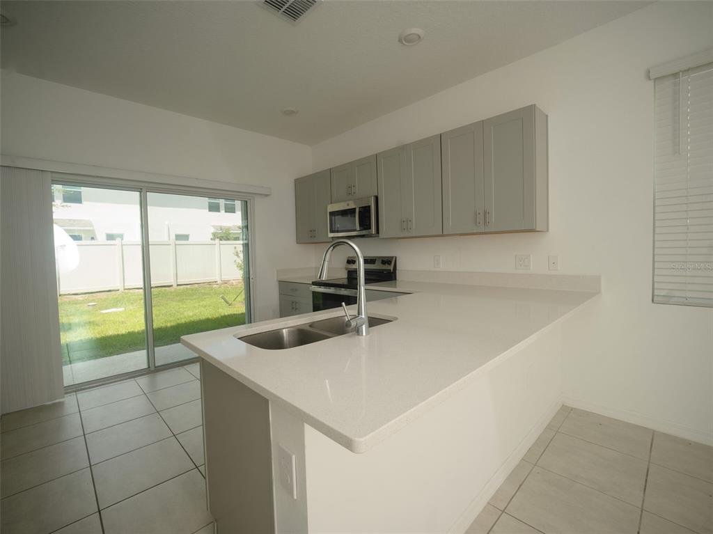A kitchen features light gray cabinets, white countertops, a stainless steel sink, and sliding glass doors — 3208 SKYLINE LOOP, POINCIANA, FL