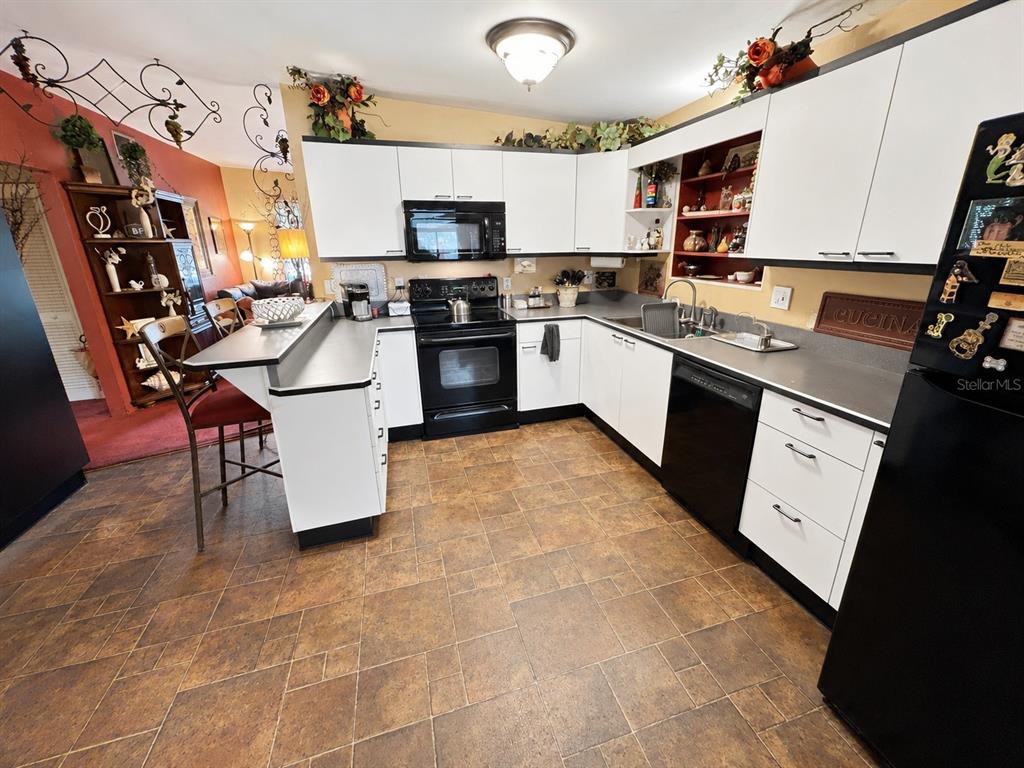 A kitchen features white cabinets, black appliances, a breakfast bar, and brown tile flooring — 608 DIXIE LANE, SOUTH DAYTONA, FL