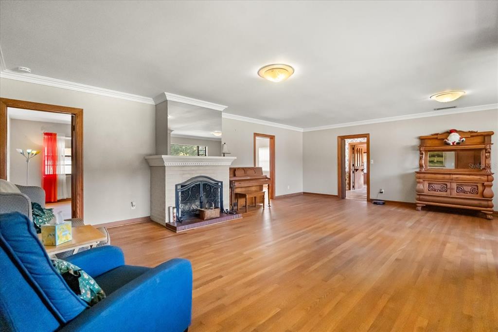 A spacious living room features hardwood floors, a brick fireplace, and a wooden piano — 205 SURPRISE DRIVE, WINTER GARDEN, FL