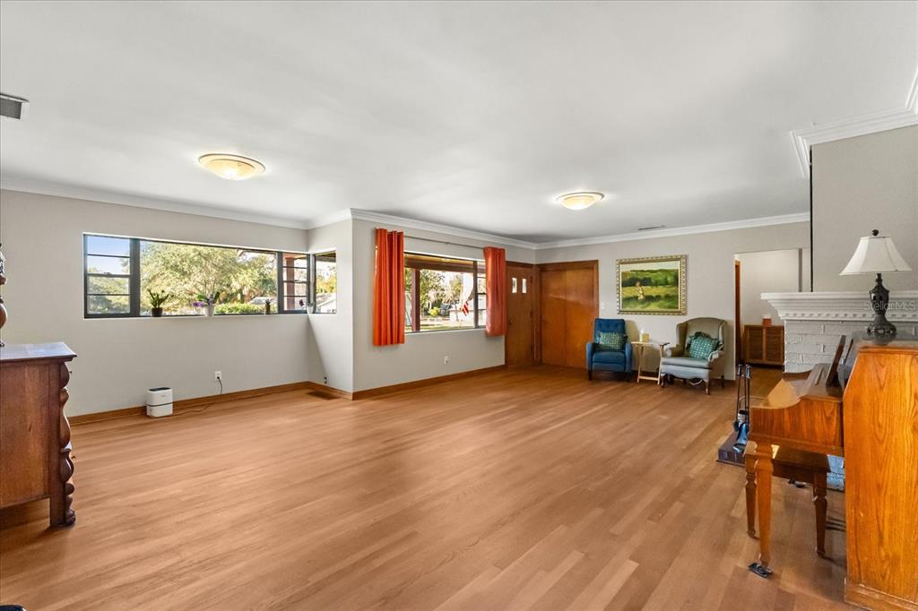 A spacious living room features hardwood floors, large windows with orange curtains, and a piano — 205 SURPRISE DRIVE, WINTER GARDEN, FL