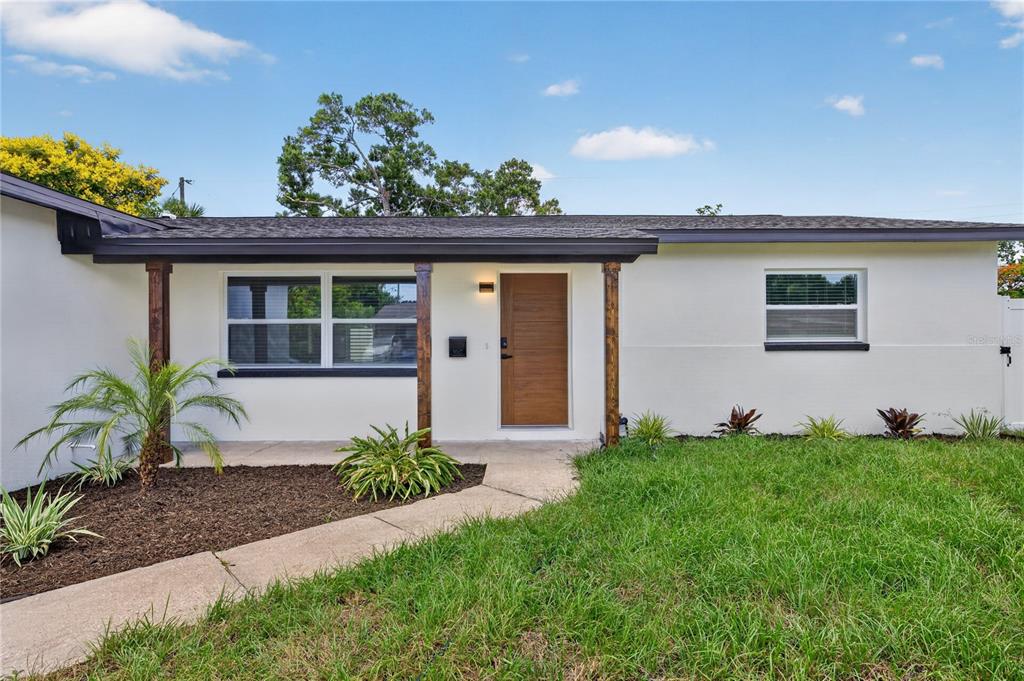 A single-story house exterior features a white facade, a wood-grain front door, and dark trim — 2091 62ND PLACE S, ST PETERSBURG, FL