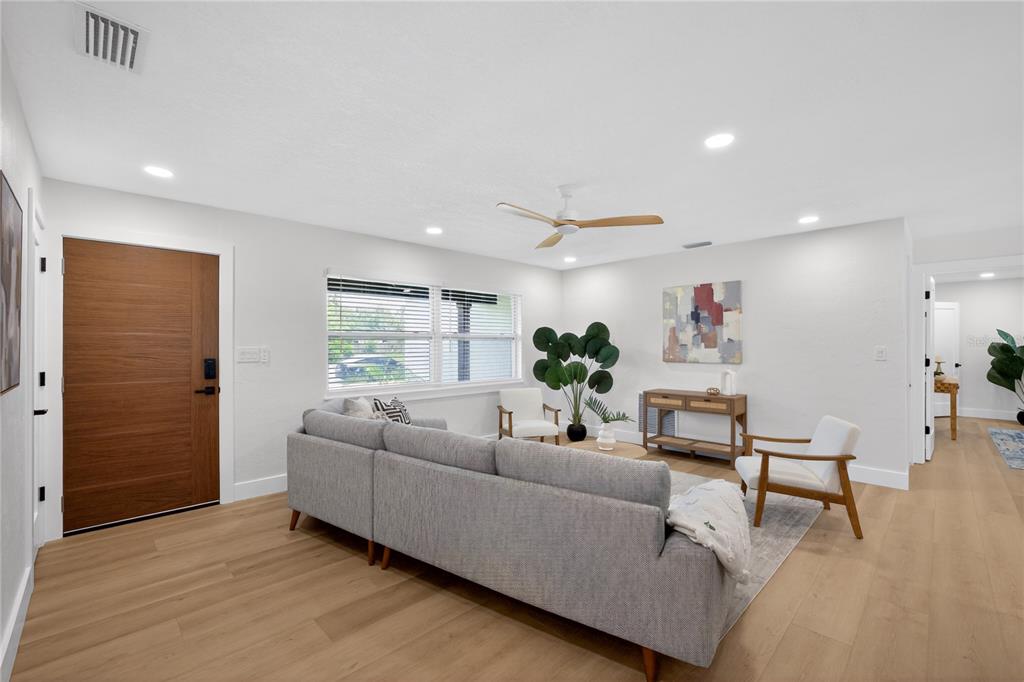 A living room features a gray sectional sofa, two white chairs, and light wood flooring — 2091 62ND PLACE S, ST PETERSBURG, FL