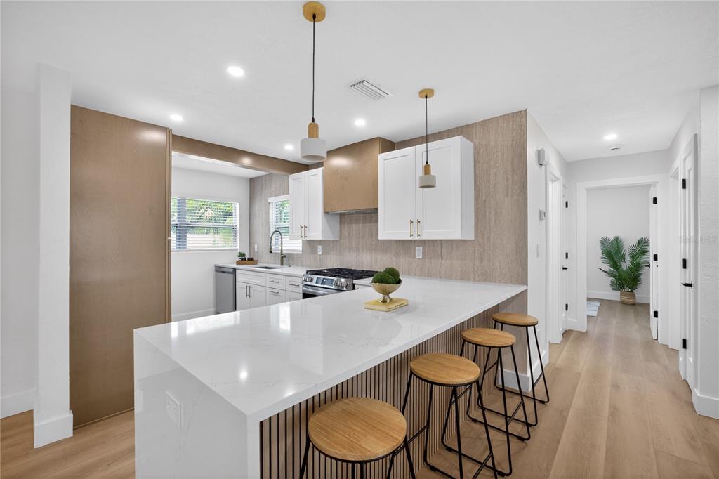 A modern kitchen features white cabinetry, a waterfall island with bar stools, and wood-look flooring — 2091 62ND PLACE S, ST PETERSBURG, FL