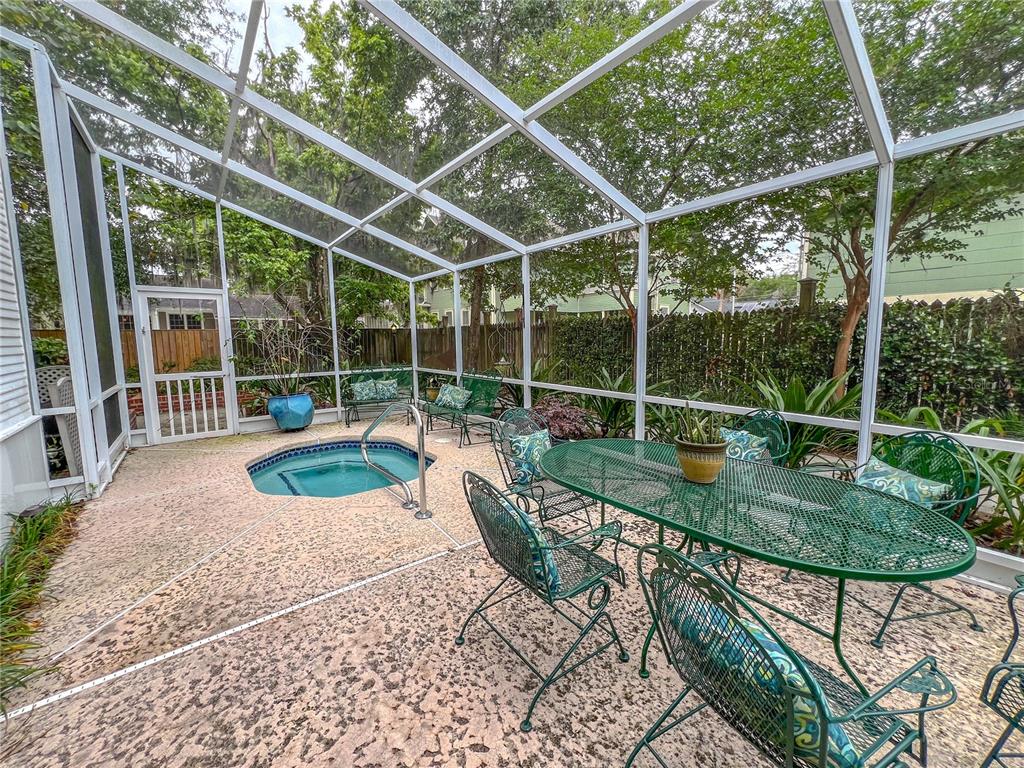 A screened-in patio features a small built-in spa, metal patio furniture, and concrete flooring — 516 NE 4TH STREET, GAINESVILLE, FL