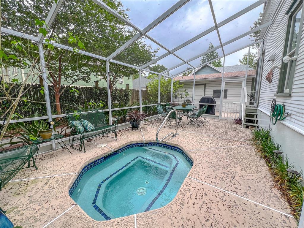 A screened-in patio features a built-in hot tub, patio furniture, and concrete flooring — 516 NE 4TH STREET, GAINESVILLE, FL
