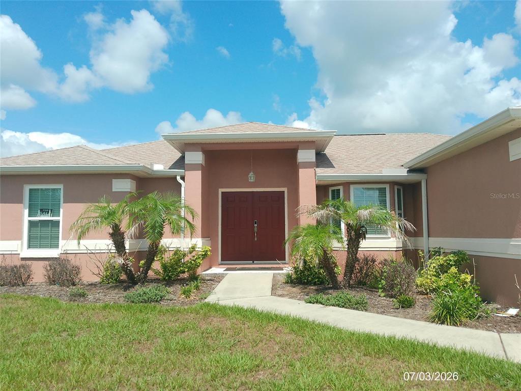 The exterior of a single-story house features a red double front door and palm trees — 3273 PEBBLEBROOKE BOULEVARD, LAKELAND, FL