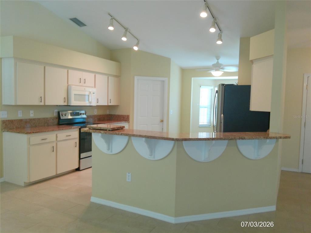 A kitchen with light cabinets, granite countertops, a breakfast bar, and track lighting — 3273 PEBBLEBROOKE BOULEVARD, LAKELAND, FL