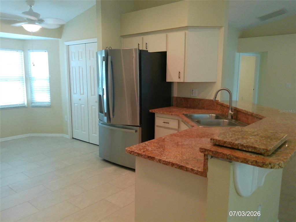 A kitchen features stainless steel appliances, white cabinets, and reddish-brown granite countertops — 3273 PEBBLEBROOKE BOULEVARD, LAKELAND, FL