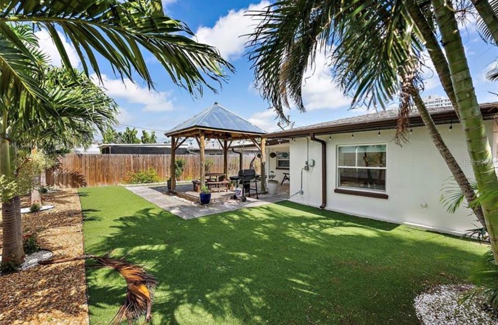 A backyard features a wooden gazebo, artificial turf, palm trees, and a white house exterior — 6750 W FLAMINGO WAY S, ST PETERSBURG, FL