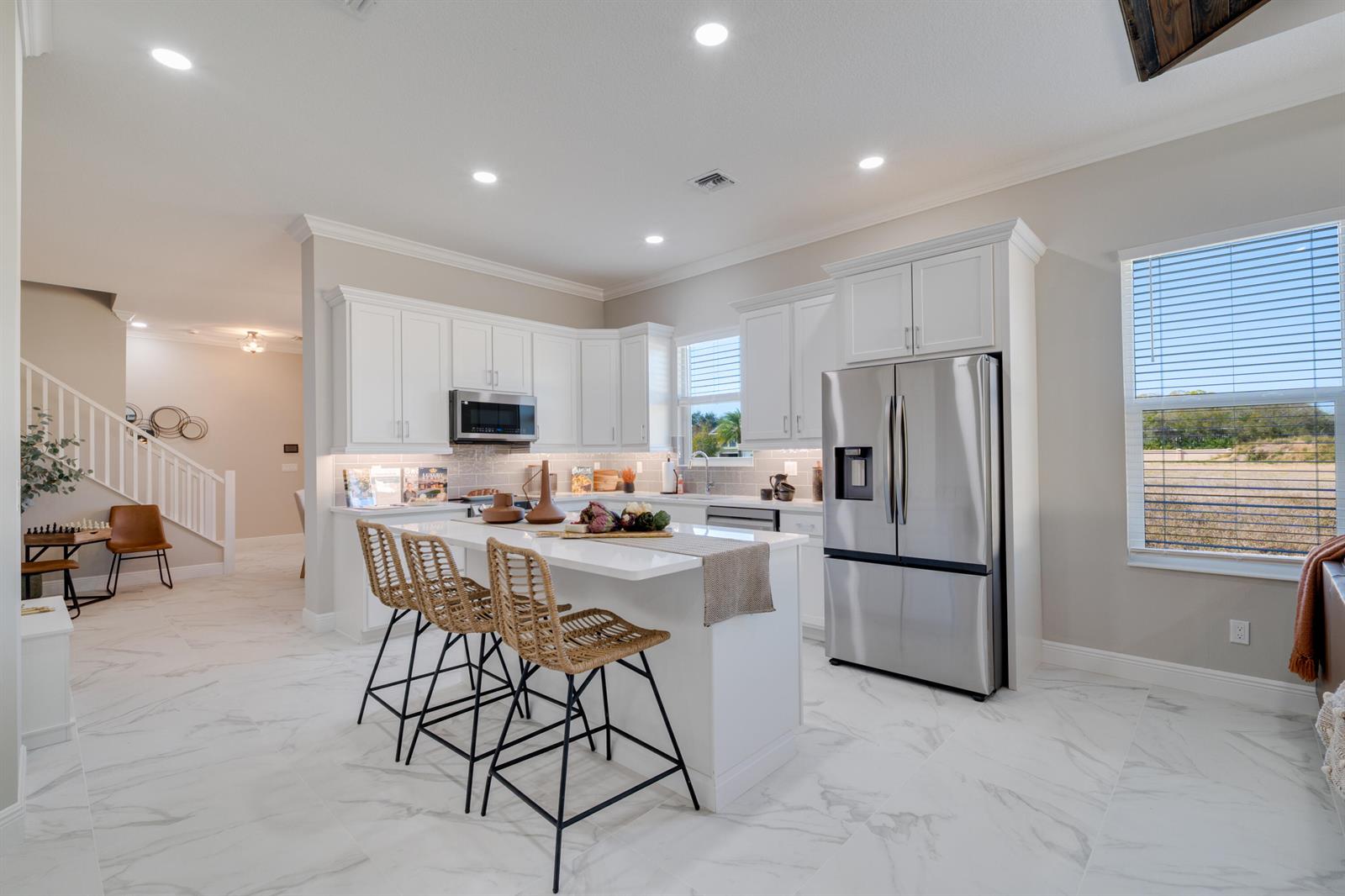 A modern kitchen features white cabinetry, a marble-topped island with wicker stools, and stainless appliances — 2005 Bridgepointe Circle # 97, Vero Beach FL 32967, VERO BEACH, FL