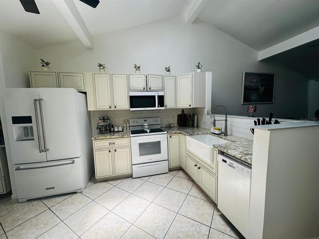 A kitchen features white cabinets, stainless steel appliances, a farmhouse sink, and granite countertops — 16004 SADDLE CREEK DRIVE, TAMPA, FL
