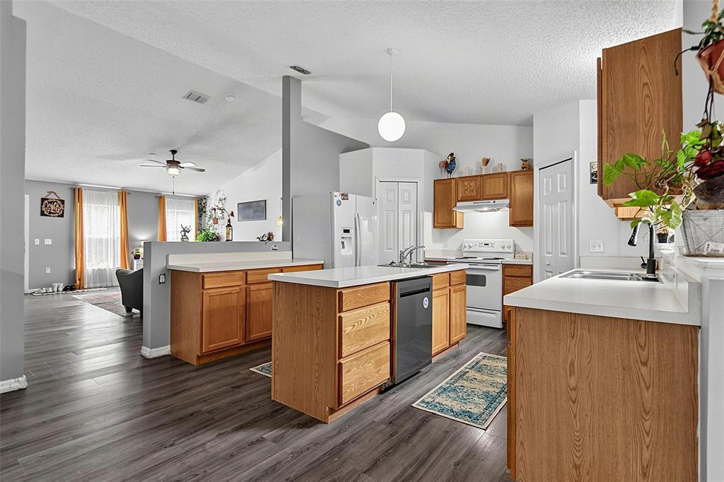 A kitchen with wood cabinets, white countertops, and a center island overlooks a living area — 30 RYDER DRIVE, PALM COAST, FL